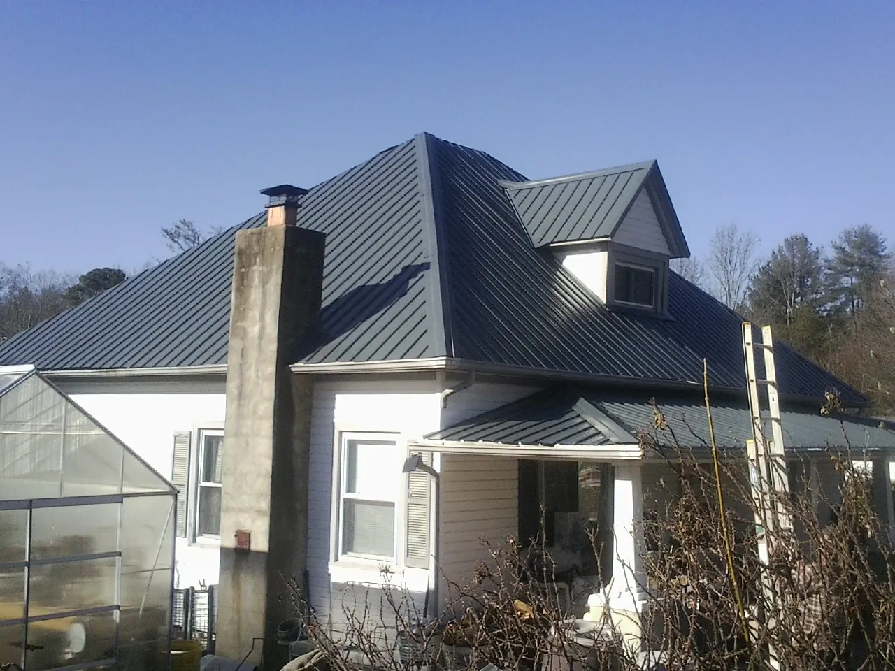Dark blue standing seam metal roof on a white farmhouse with dormer — Slate & Tile Roof Repair by Roofing Brothers in Trinity Center