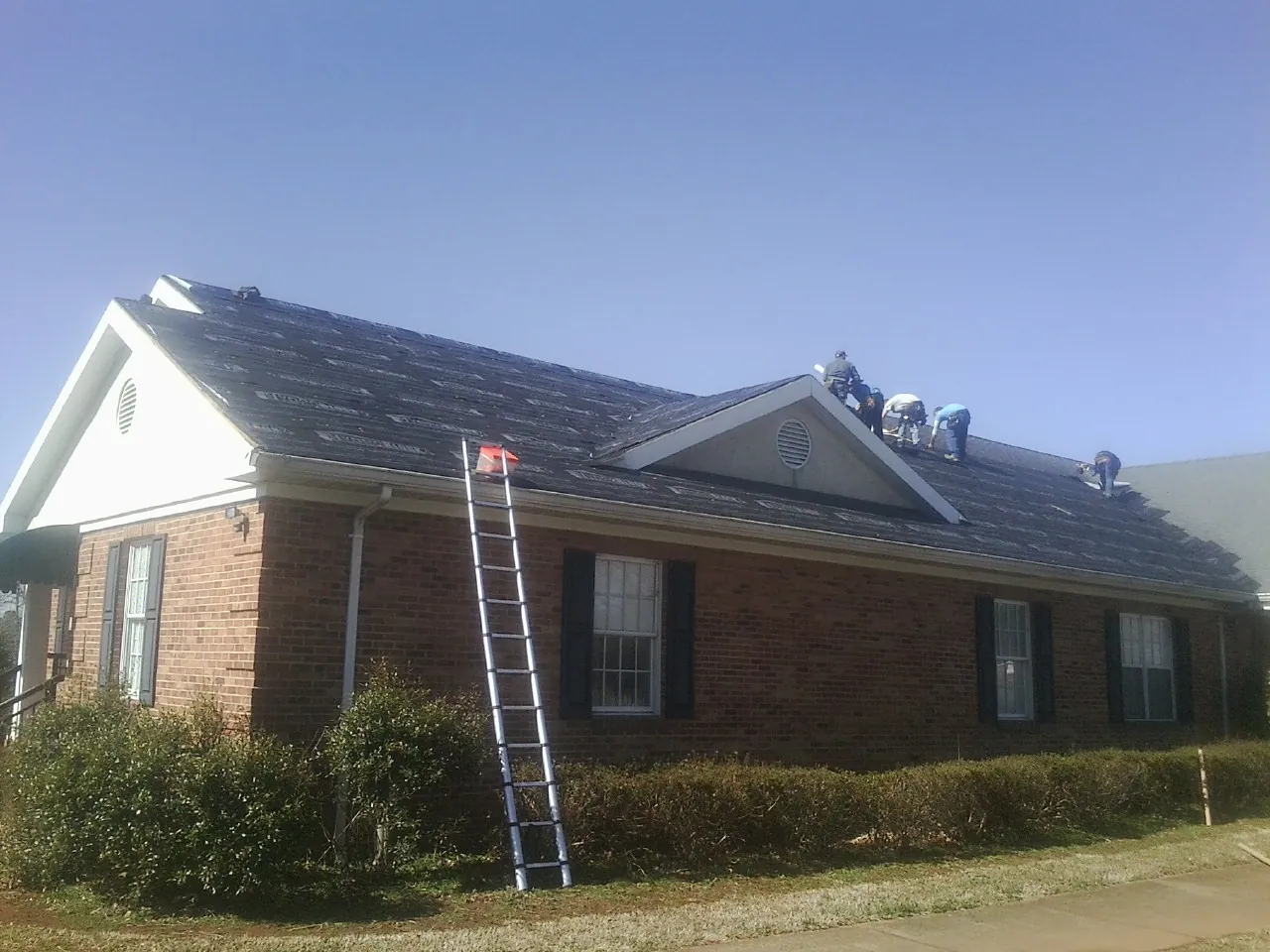 Crew tearing shingles off a brick ranch roof with a ladder set — Emergency Roof Repair work by our crew in Trinity Center