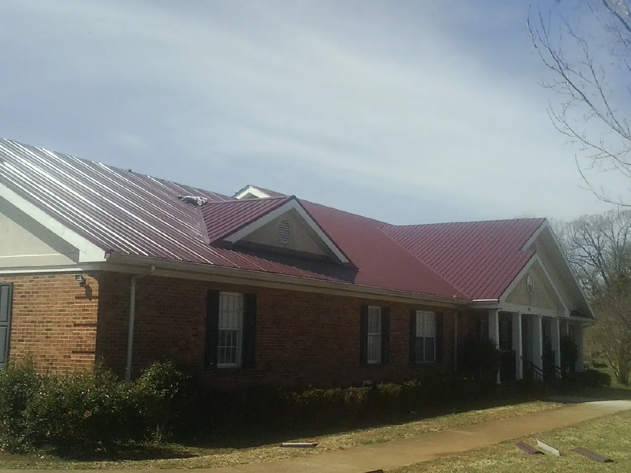 Red metal roof with gabled entries on a long brick building, from a Hail Damage Roof Repair job in Trinity Center